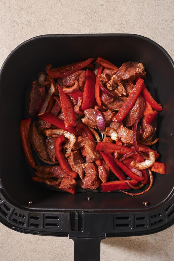 Marinated steak and bell peppers in the air fryer basket.