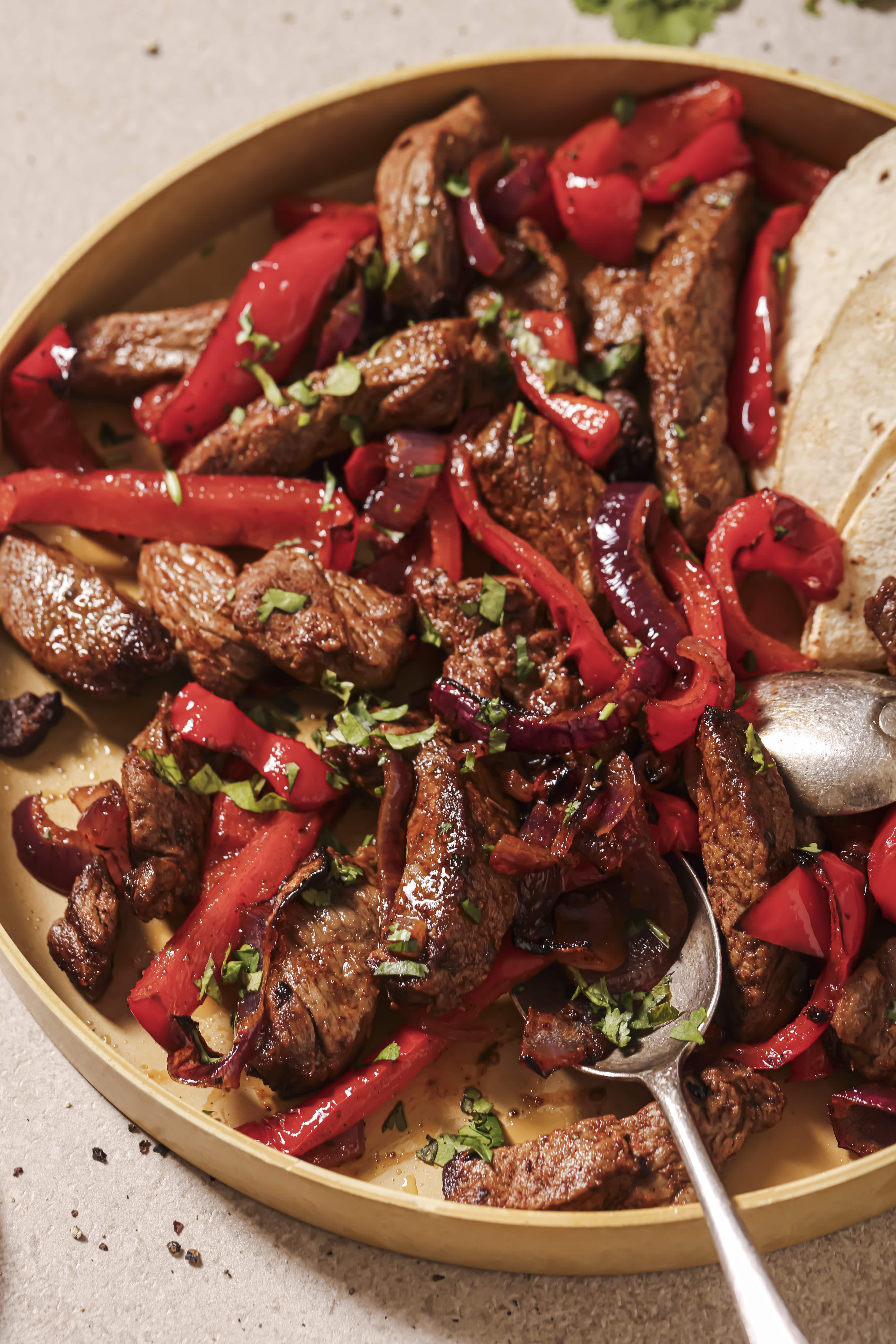 A bowl of steak fajitas served with tortillas.