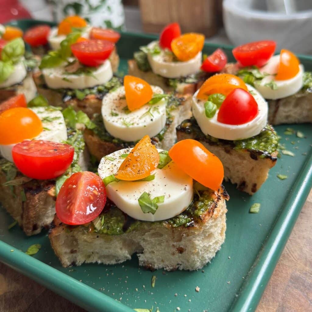 Tomato toast with mozzarella on a green sheet pan.