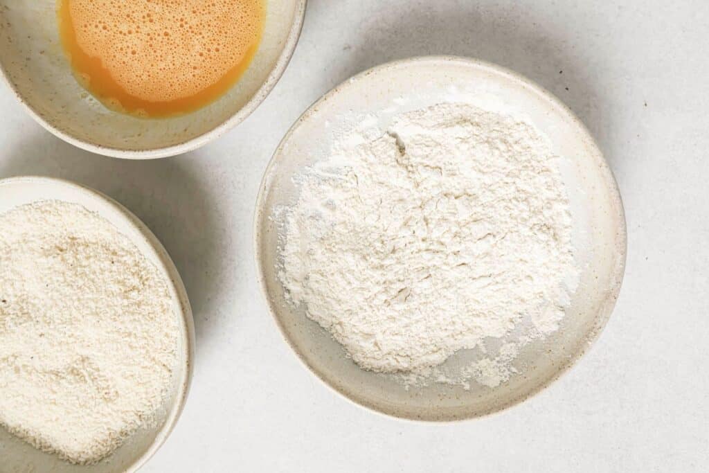 Three bowls with flour, breadcrumbs, and beaten eggs.