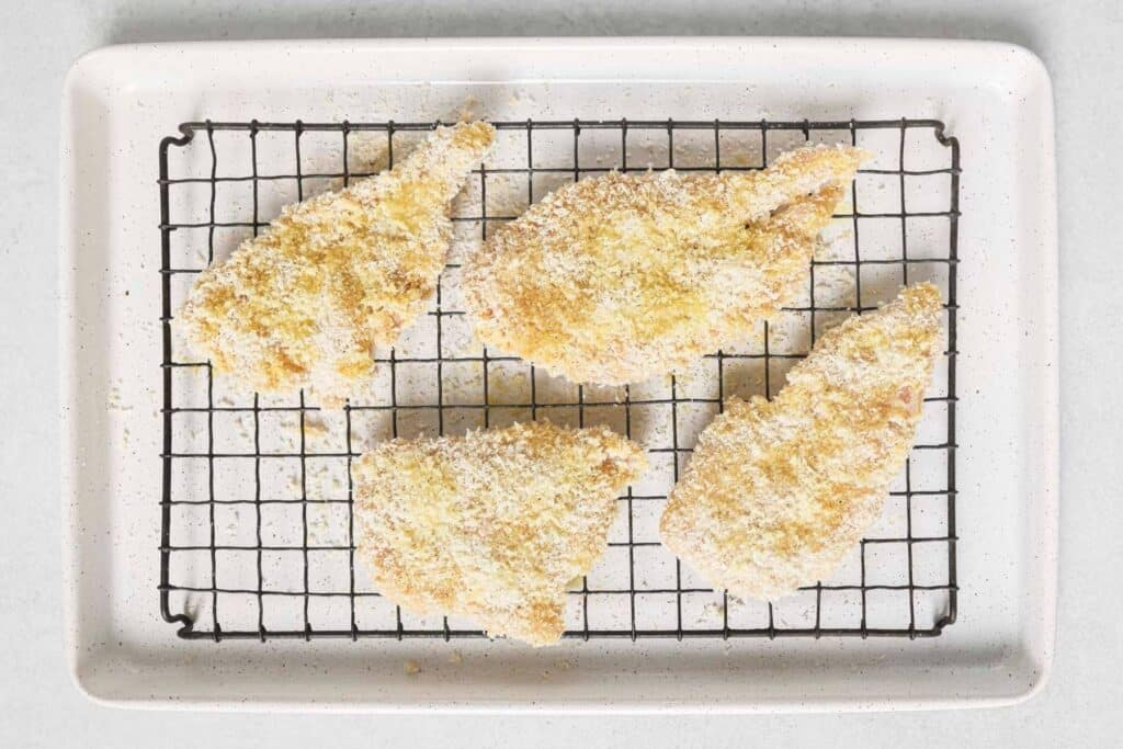 Breaded chicken cutlets on a wire rack over a baking sheet.