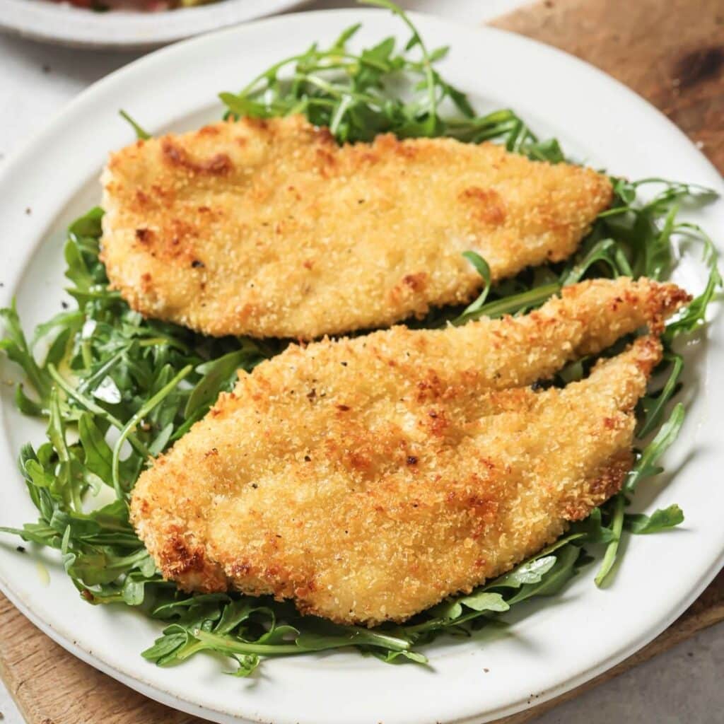 A plate of baked chicken cutlets served over arugula.