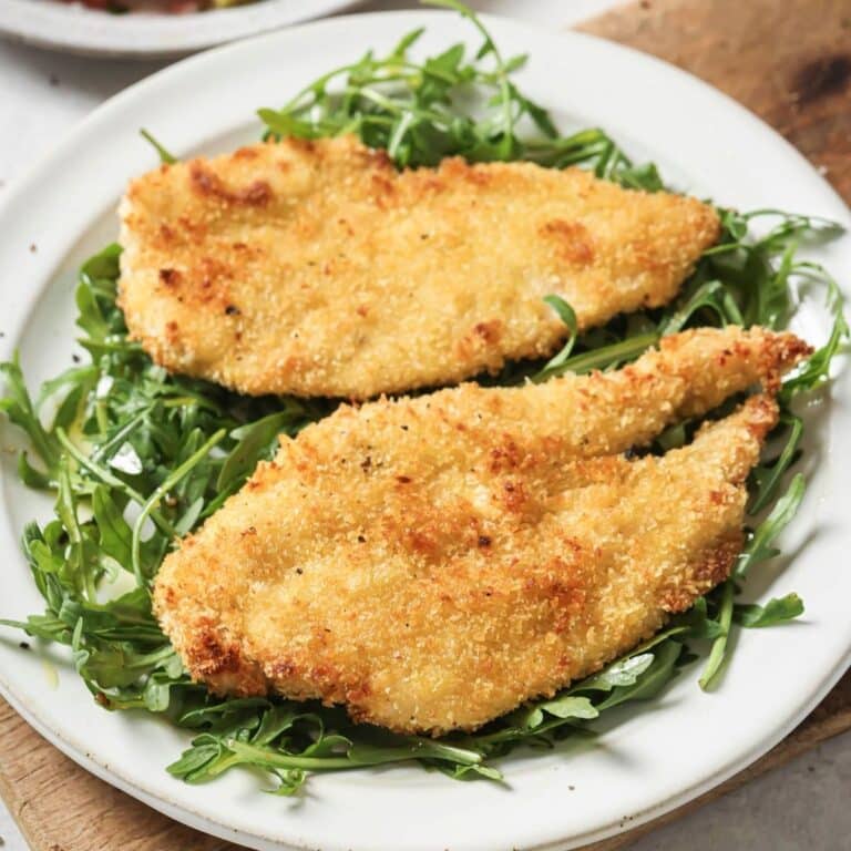 A plate of baked chicken cutlets served over arugula.