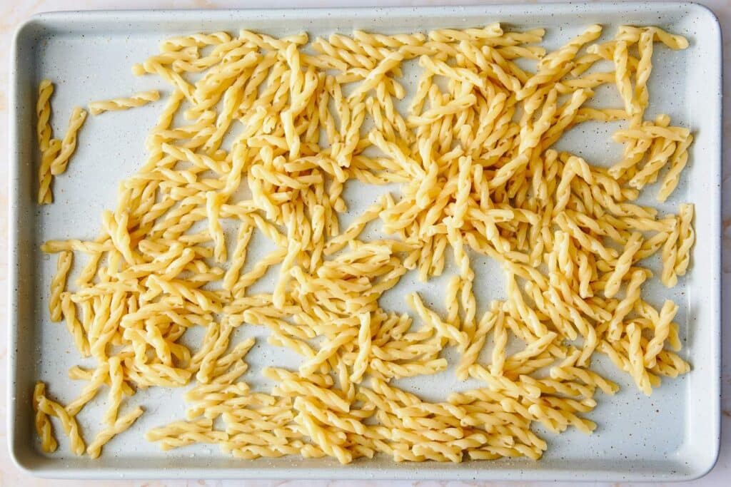 A baking sheet covered with cooked pasta.