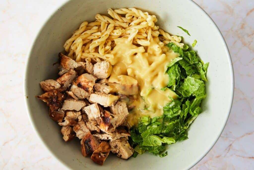 Combining pasta salad ingredients in a large bowl.