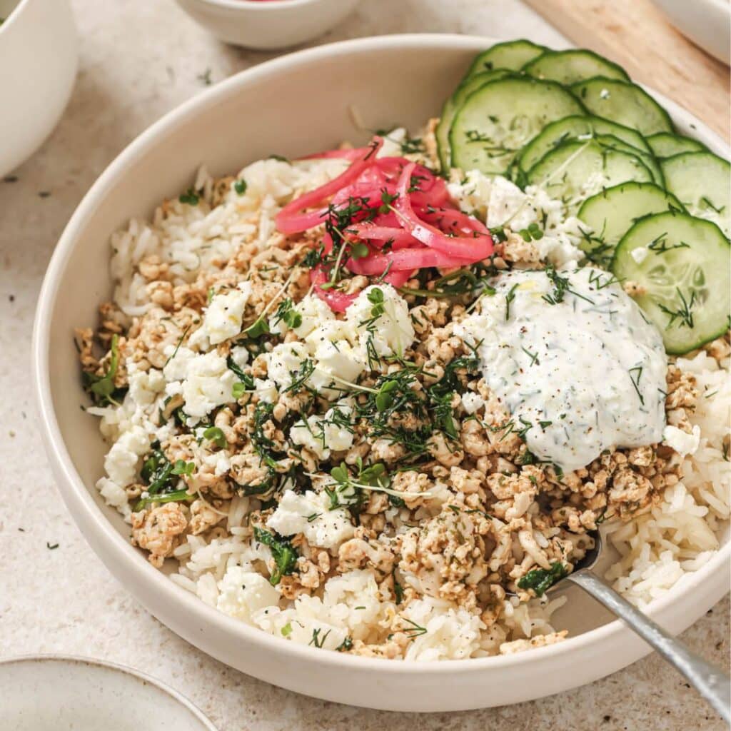 A greek chicken rice bowl topped with cucumbers, pickled onion, and tzatziki.