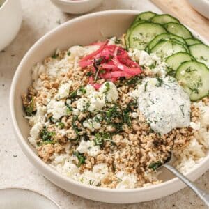 A greek chicken rice bowl topped with cucumbers, pickled onion, and tzatziki.