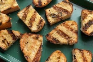 Grilled pieces of sourdough bread on a green sheet pan.