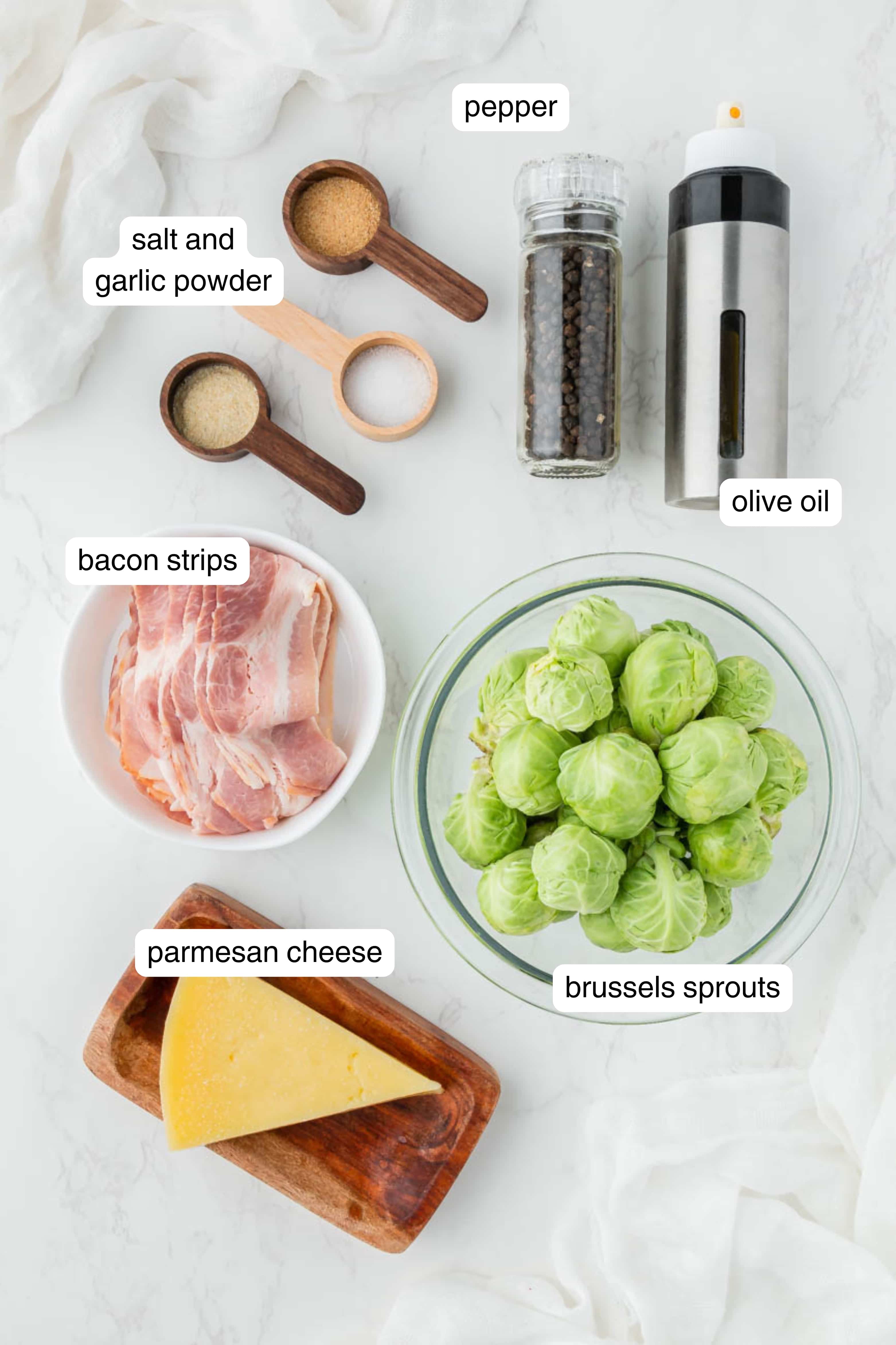 bacon, brussel sprouts, parmesan cheese, salt, garlic powder, and pepper laid out on a marble counter