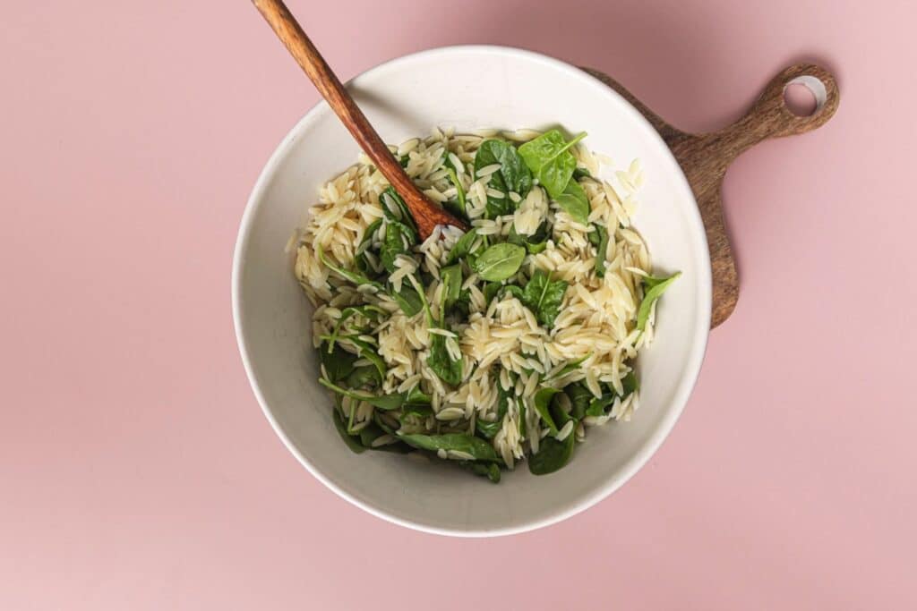 Mixing orzo with spinach.