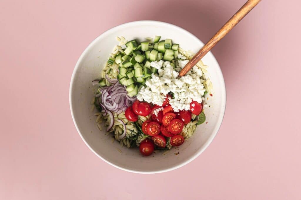 Mixing ingredients for orzo pasta salad in a large bowl.