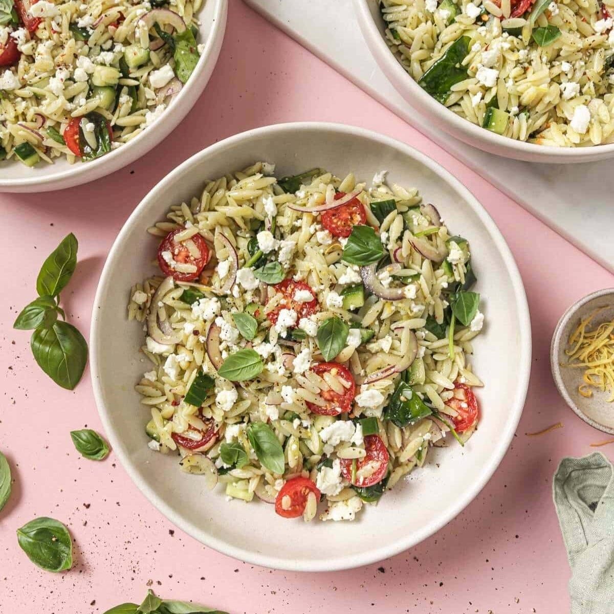 Three bowls of orzo pasta salad with spinach.