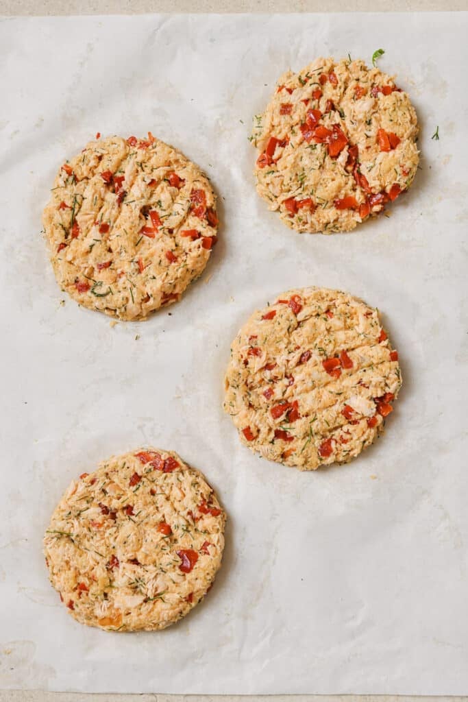 Uncooked salmon burgers assembled on a baking sheet with parchment paper.