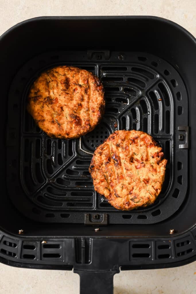 Cooked salmon burgers in a black air fryer basket.