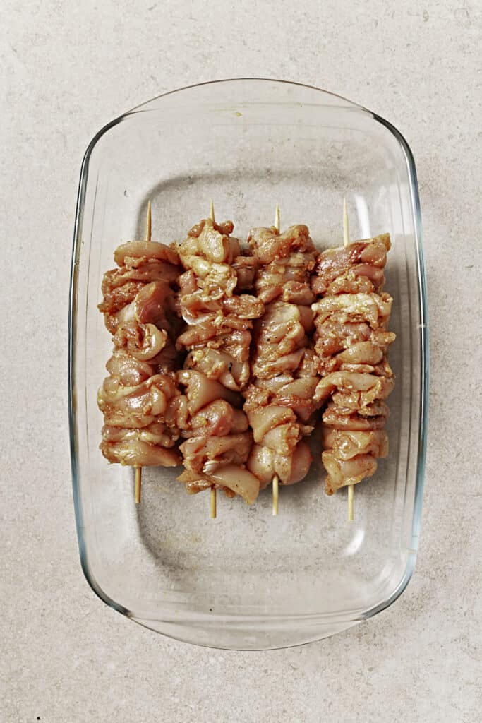 Raw chicken on four skewers sitting in a glass dish