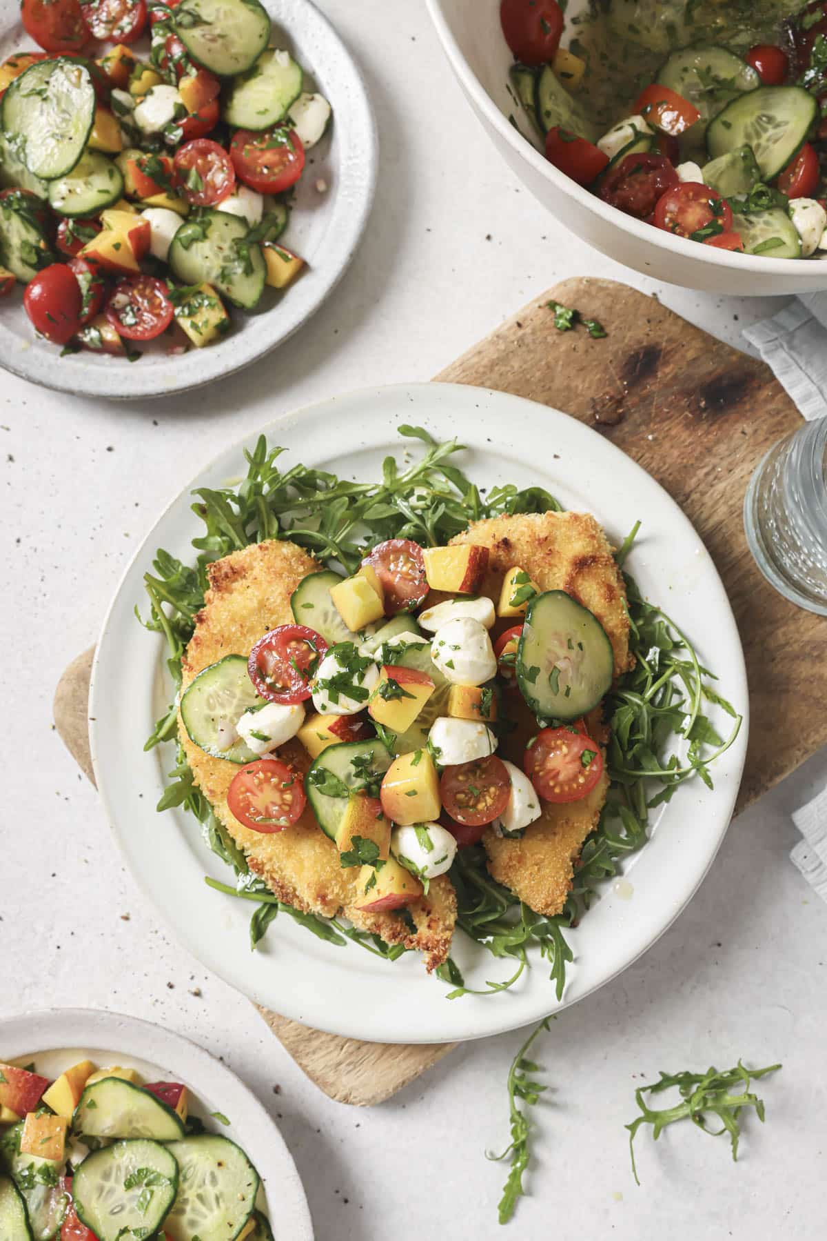 Baked chicken cutlets on a white plate with arugula and topped with a cherry tomato salad.