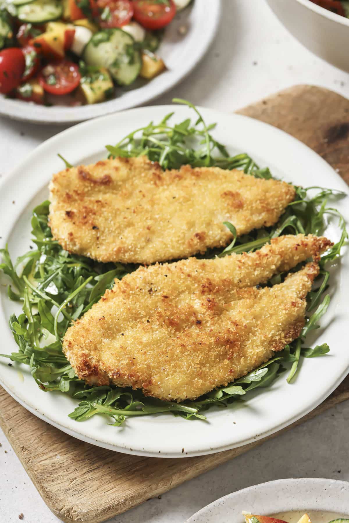 Two baked chicken cutlets on a white plate with arugula.