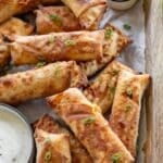 A tray filled with crispy golden brown buffalo chicken egg rolls, garnished with sliced green onions and served with dipping bowls of ranch and buffalo sauce. These 30-minute air fryer chicken egg rolls are stuffed with spicy shredded chicken and cheese for a flavorful, crowd-pleasing appetizer.