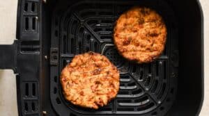 Two cooked salmon patties in an air fryer basket.