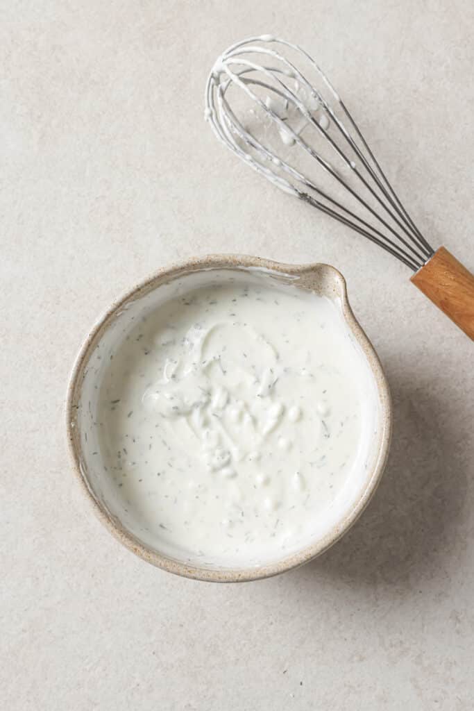 Dressing for dill pickle pasta in a small bowl near a whisk.