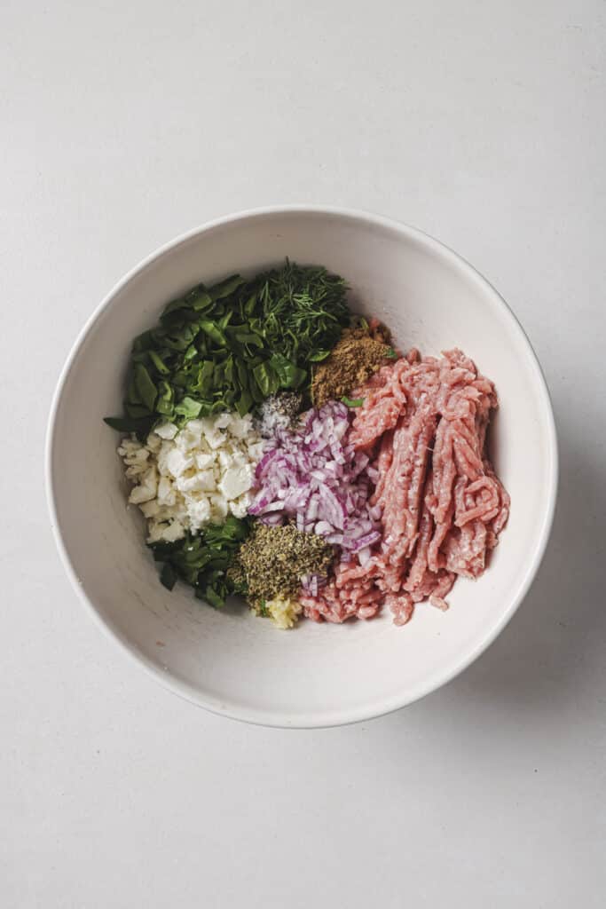 Mixing ground turkey with herbs and seasonings in a white bowl.