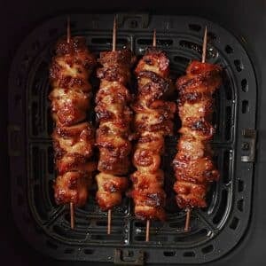 Cooked chicken thighs on skewers in an air fryer basket.