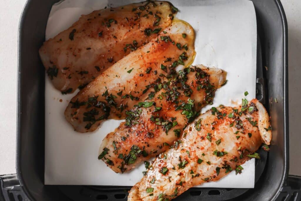Seasoned tilapia filets in the air fryer basket.