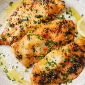 Three air fryer tilapia filets on a plate with lemon.