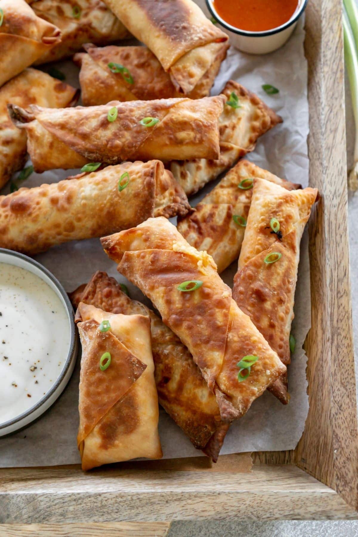 Buffalo chicken eggrolls on a platter with sauce.