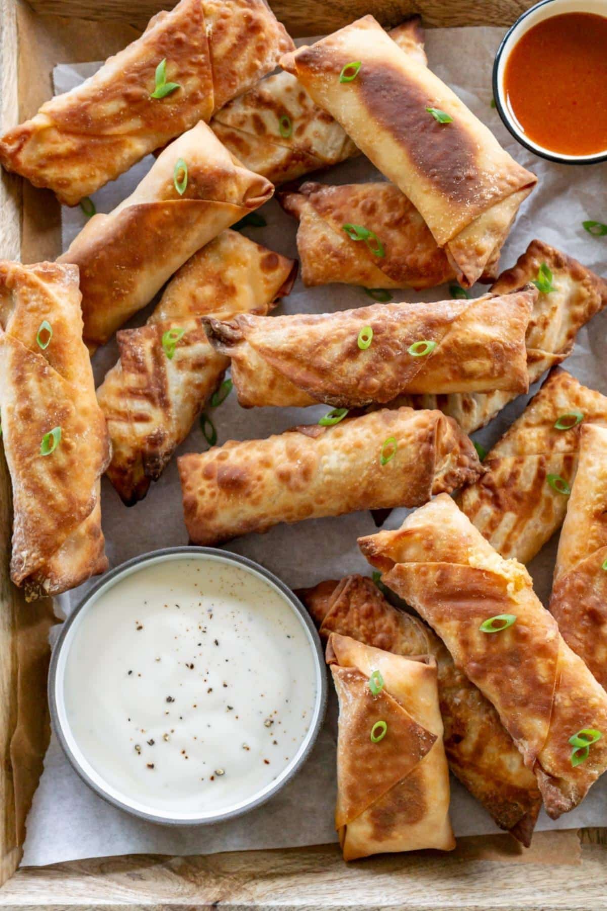Buffalo chicken egg rolls on a platter with sauce.