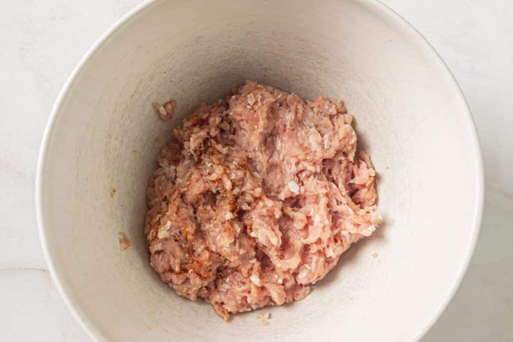 Seasoning ground chicken in a mixing bowl.