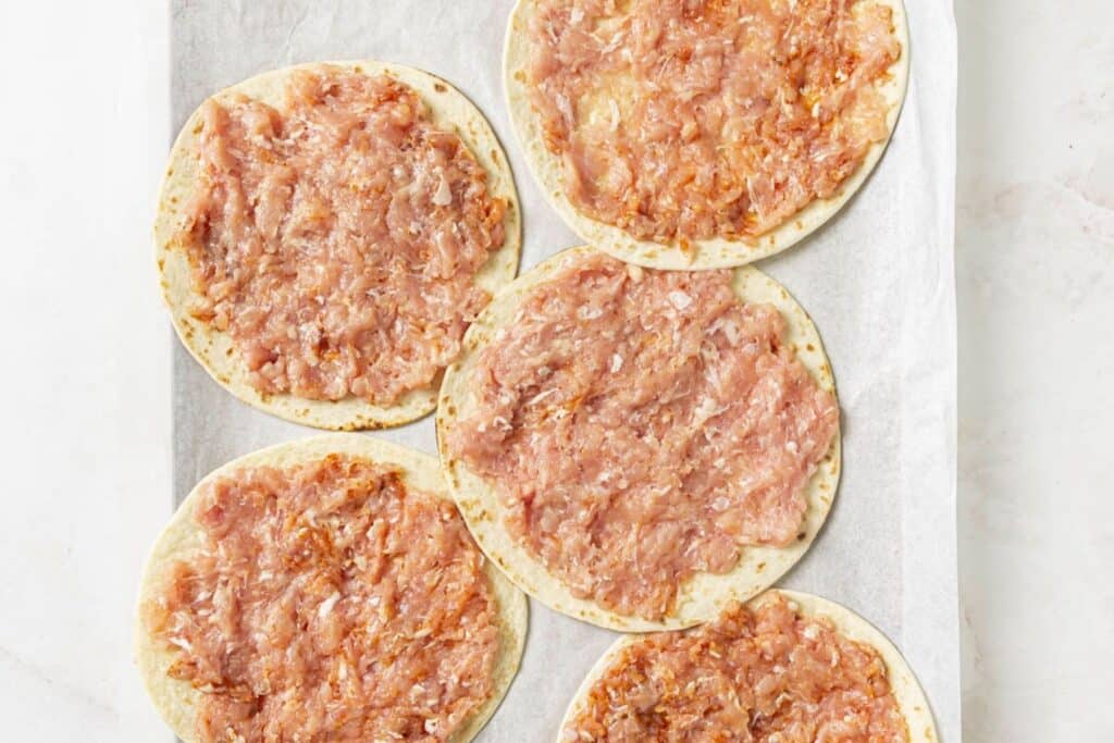 Adding ground chicken to flour tortillas.