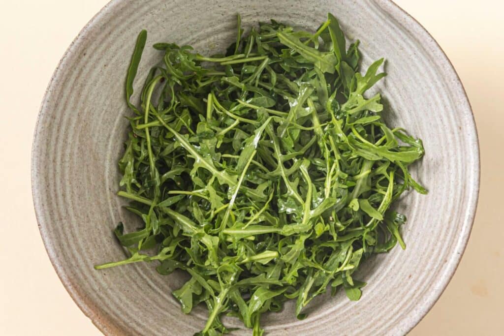 Preparing arugula salad in a bowl.