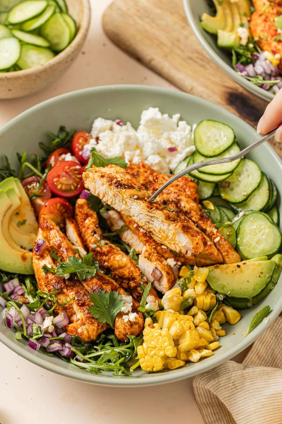 Picking up a piece of grilled chicken from a salad bowl.