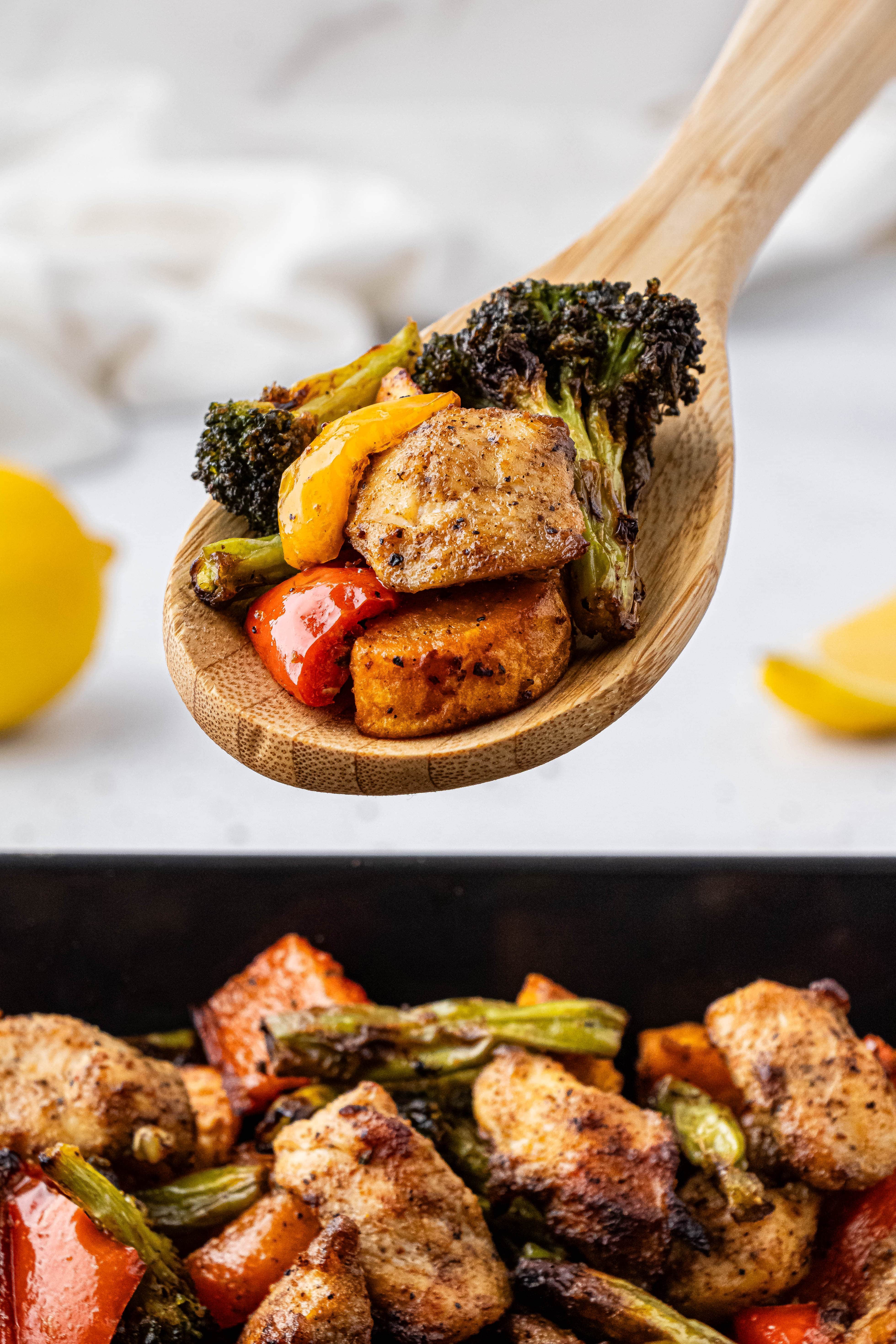 a wooden spoon with chicken, broccoli, and bell peppers