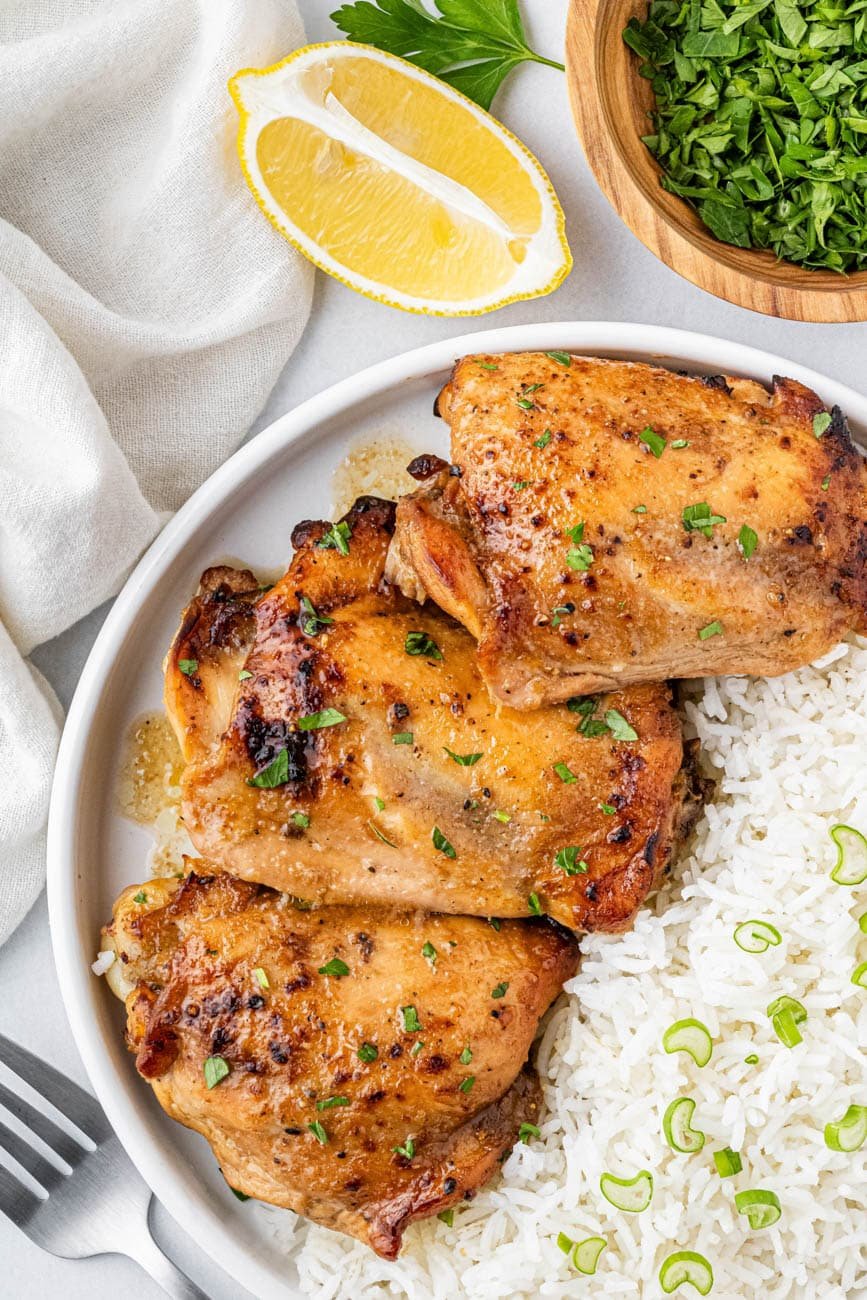 air fryer marinated chicken thighs on a white plate with rice and a lemon wedge on the side