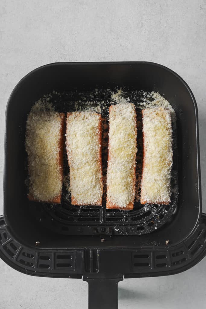 Four pieces of salmon with panko breadcrumbs and olive oil on top in a black air fryer basket.