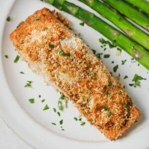 Cooked panko salmon on a white plate with asparagus.