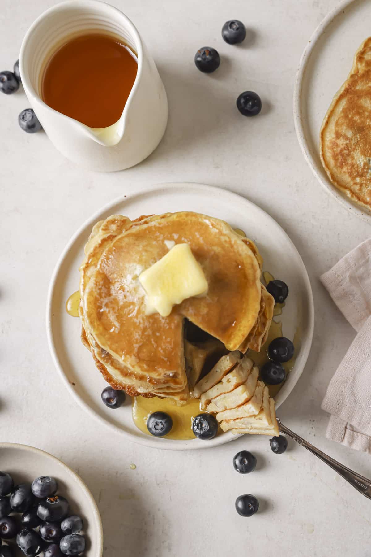 Cutting into blueberry banana pancakes on a white plate.