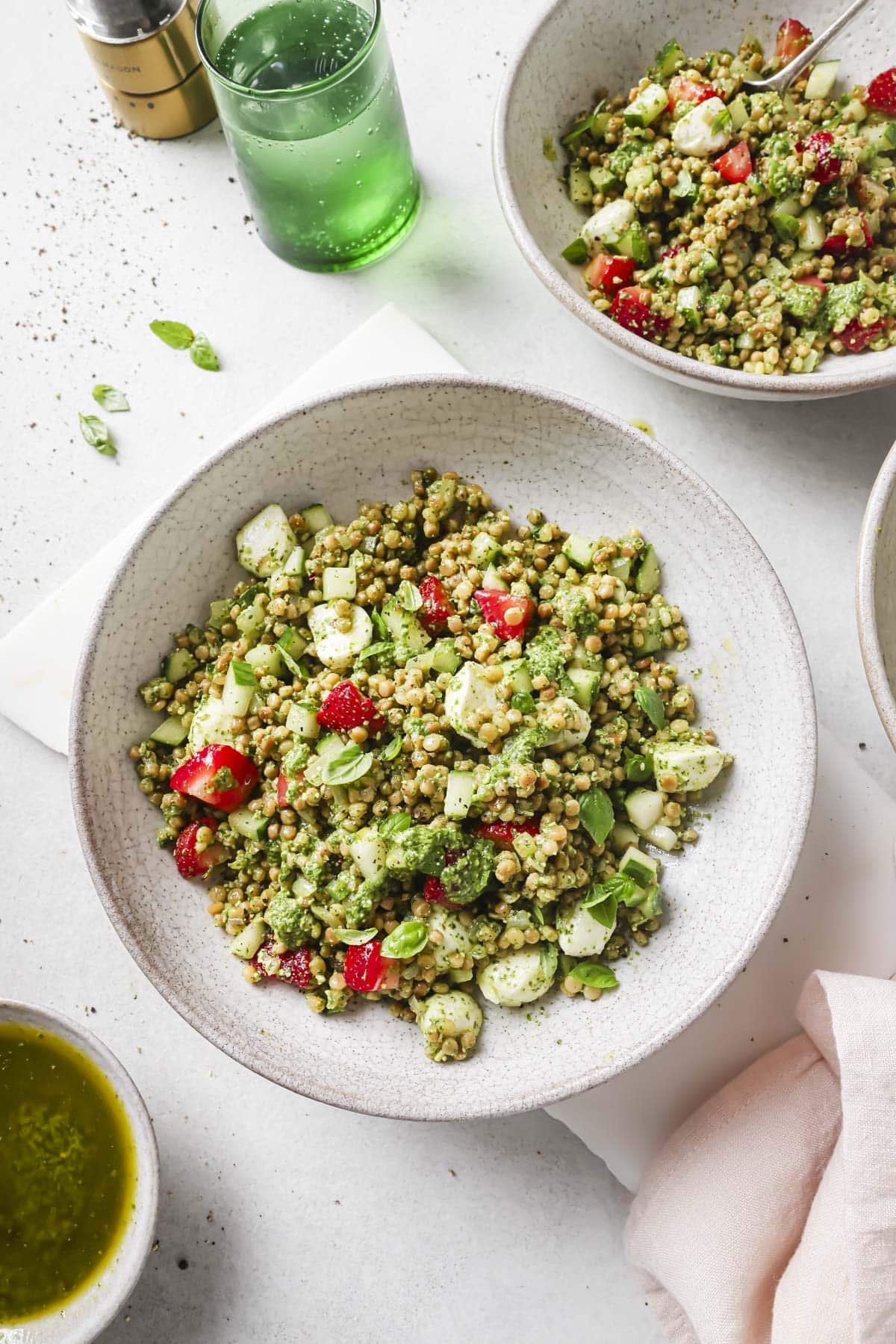 Israeli couscous salad topped with strawberries in a white bowl.