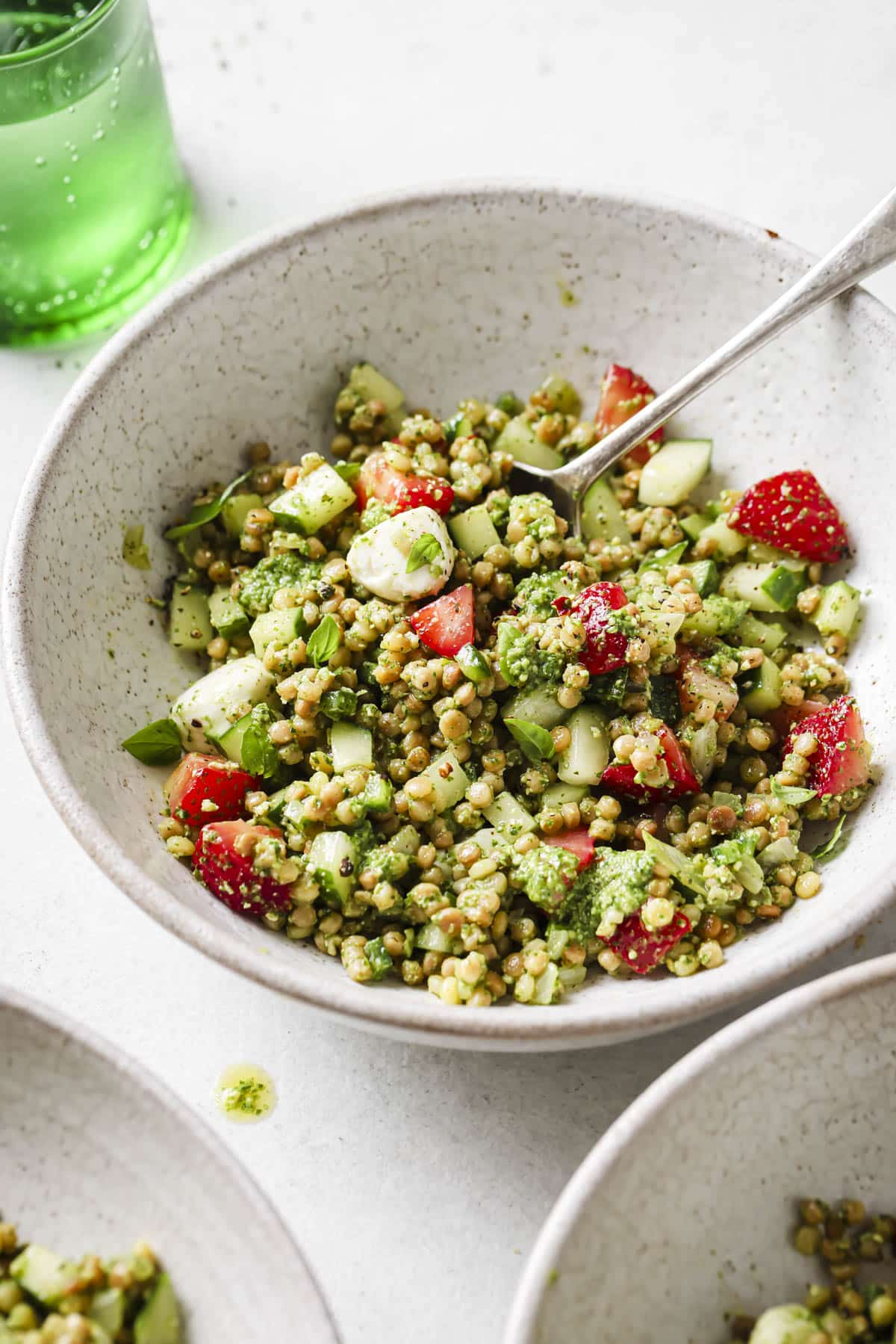 Strawberry cucumber couscous salad in a white bowl with a spoon.