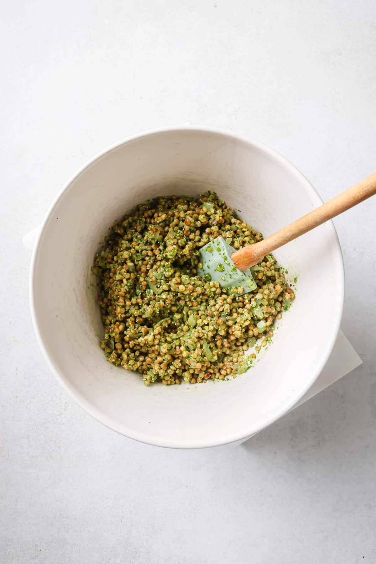 Stirring pesto dressing with couscous in a white bowl.