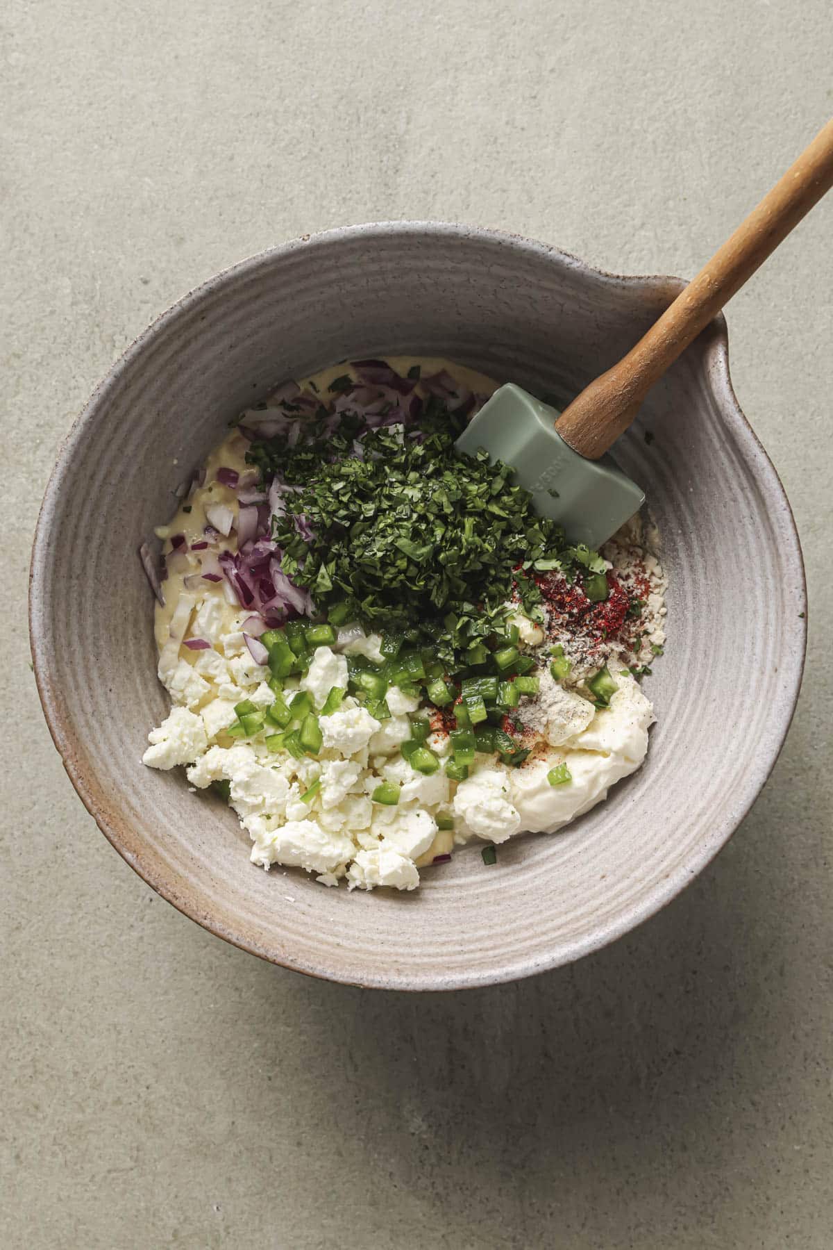 Stirring together crema cream cheese, spices, onion, and cilantro in a bowl.