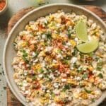 Street corn dip garnished with slices of lime.