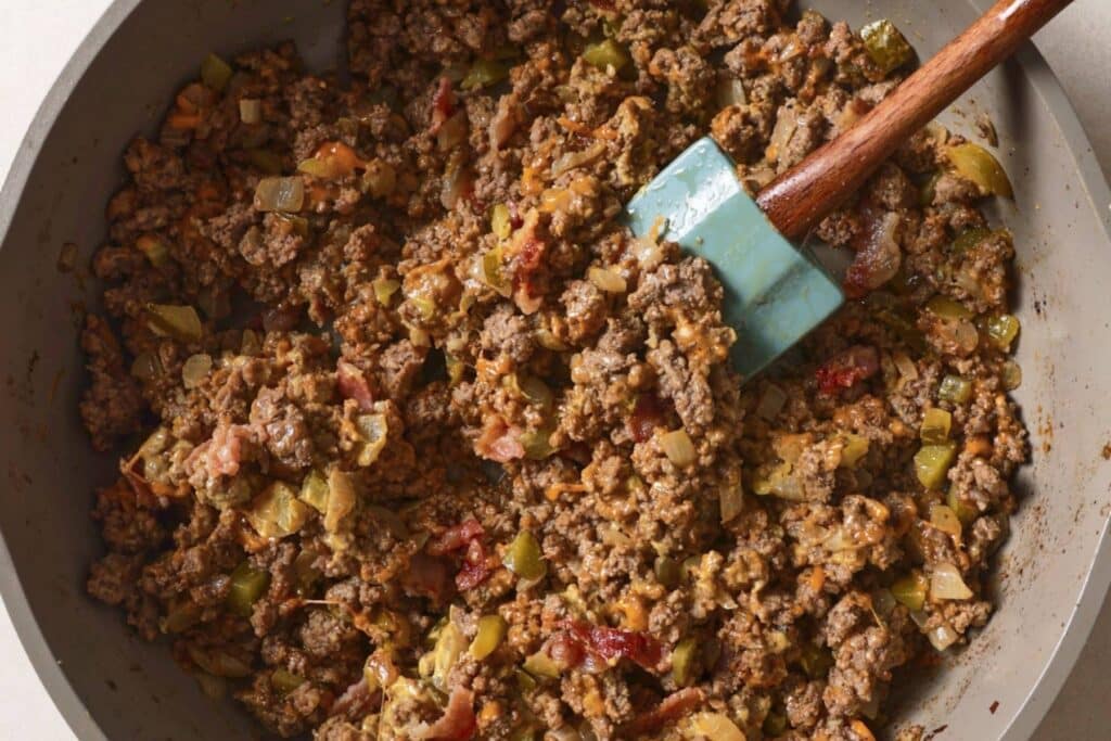 Adding cheese and bacon to ground beef in a skillet.