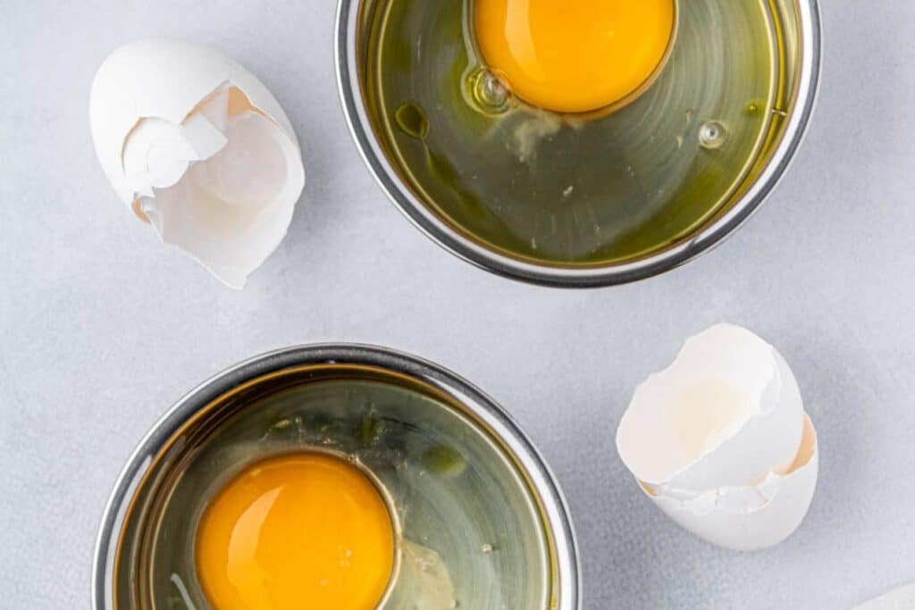 Two cracked eggs in mini muffins tins.