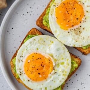 Two slices of bread with air fryer fried eggs over avocado mash.