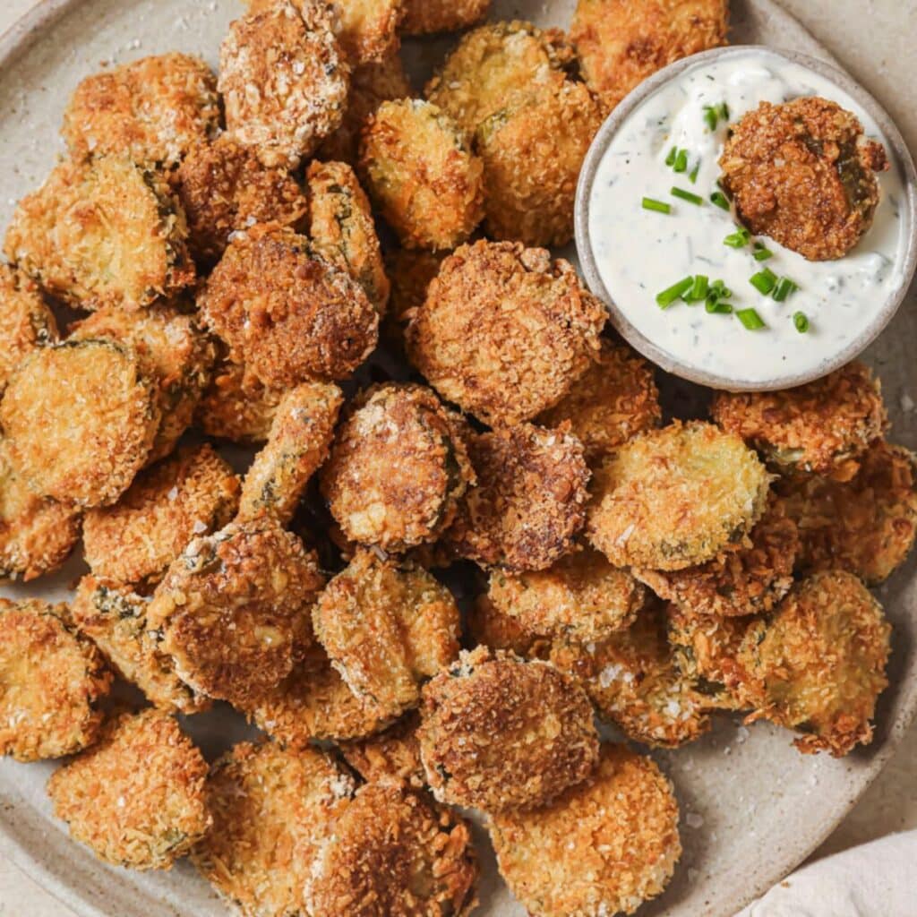 Crispy air fryer pickles on a plate with ranch dipping sauce in a cup.