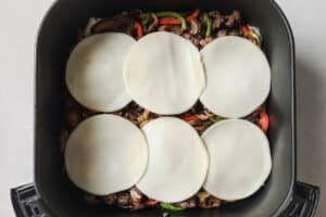 Adding provolone cheese to steak and veggies in the air fryer.