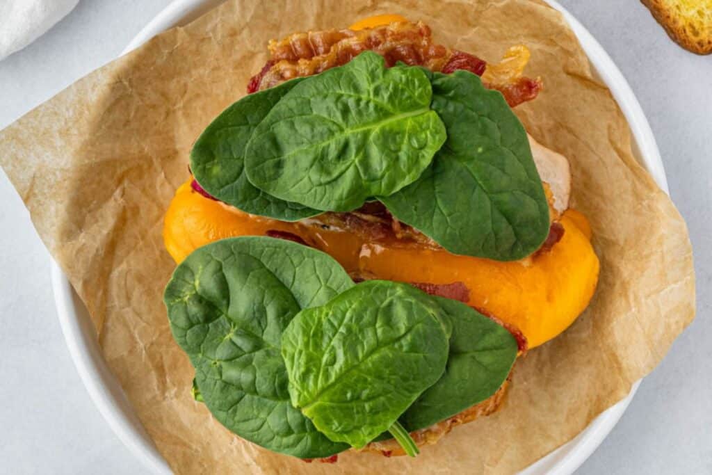 Adding spinach to an air fryer turkey sandwich.